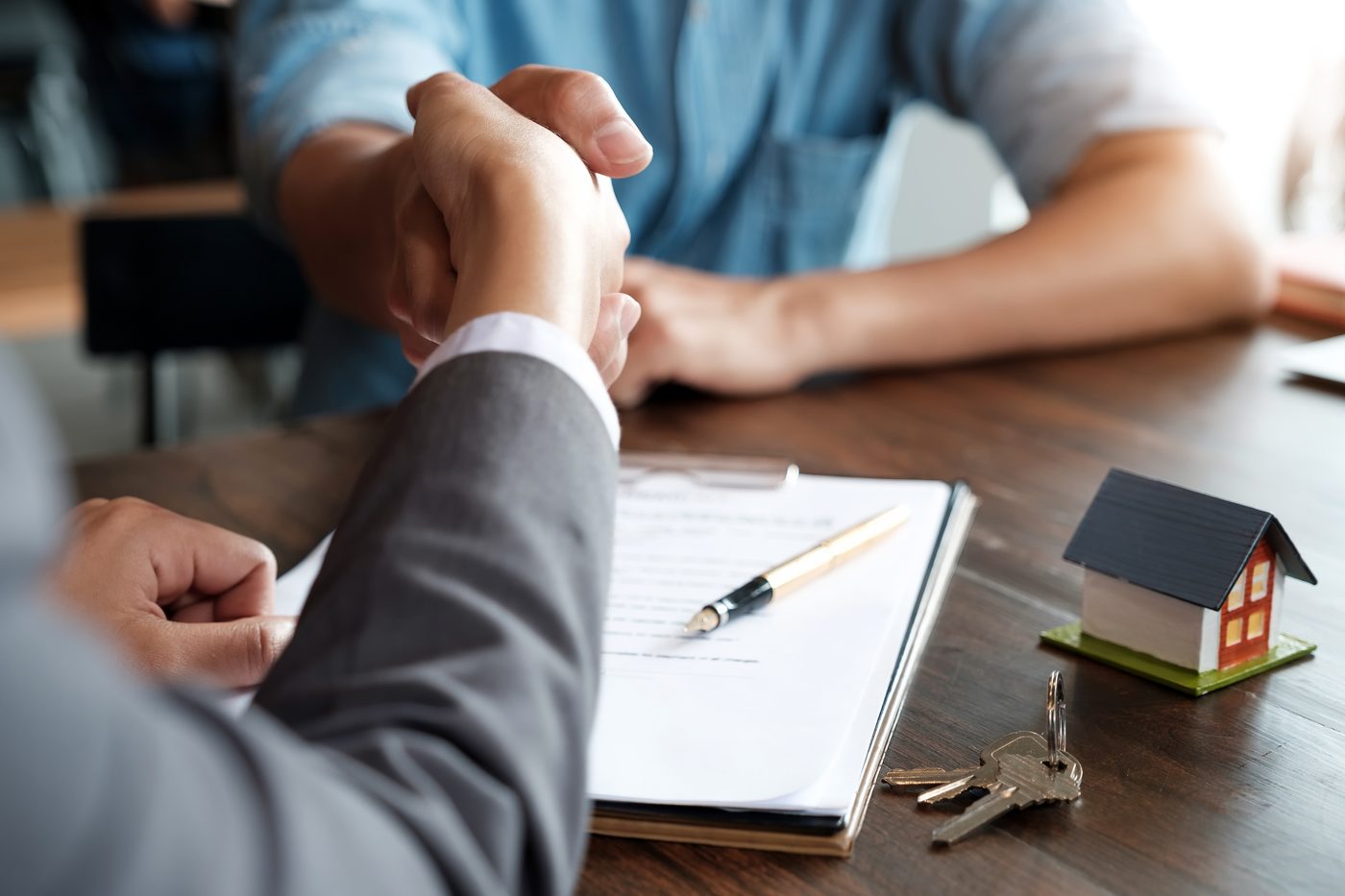 Two people shaking hands over a lease with keys and a small house model, a moment to review DADU rental expenses