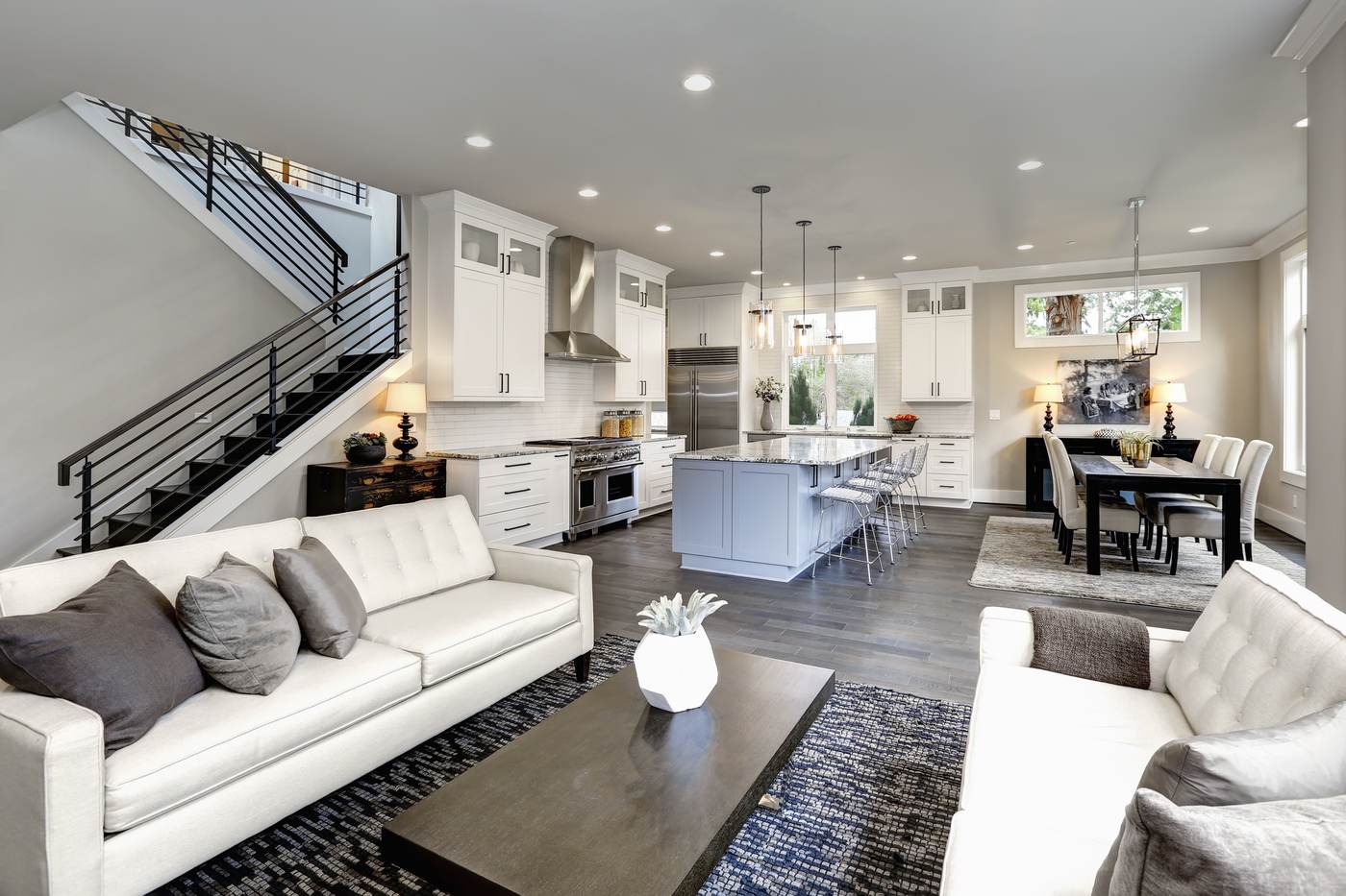 Calm open living room with white sofas, a staircase and a kitchen beyond