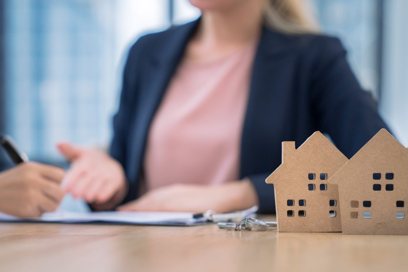 Person signing paperwork beside small wooden house models, a step in meeting Seattle RRIO requirements for a rental